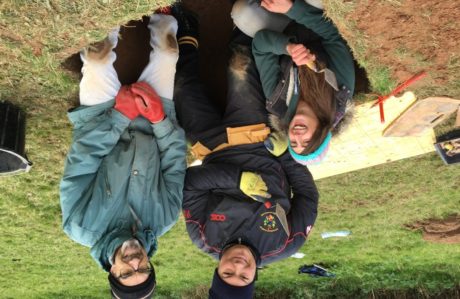 Three people huddle in a test pit, they are smiling and laughing.