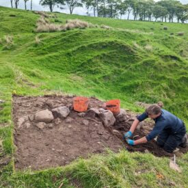 A woman digs a line of stones in a trench