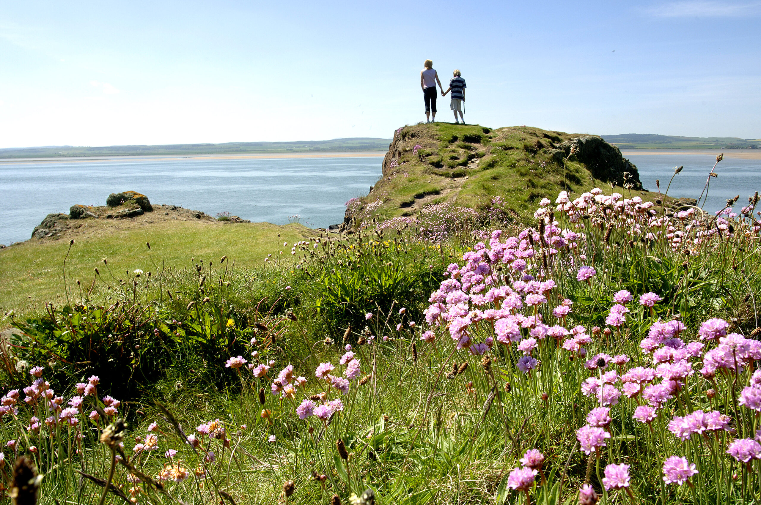 Two people stand on a scenic hill looking out to sea